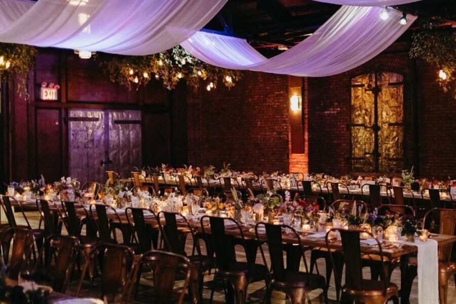 Wedding reception venue with long tables decorated with candles and drapery hanging from ceiling