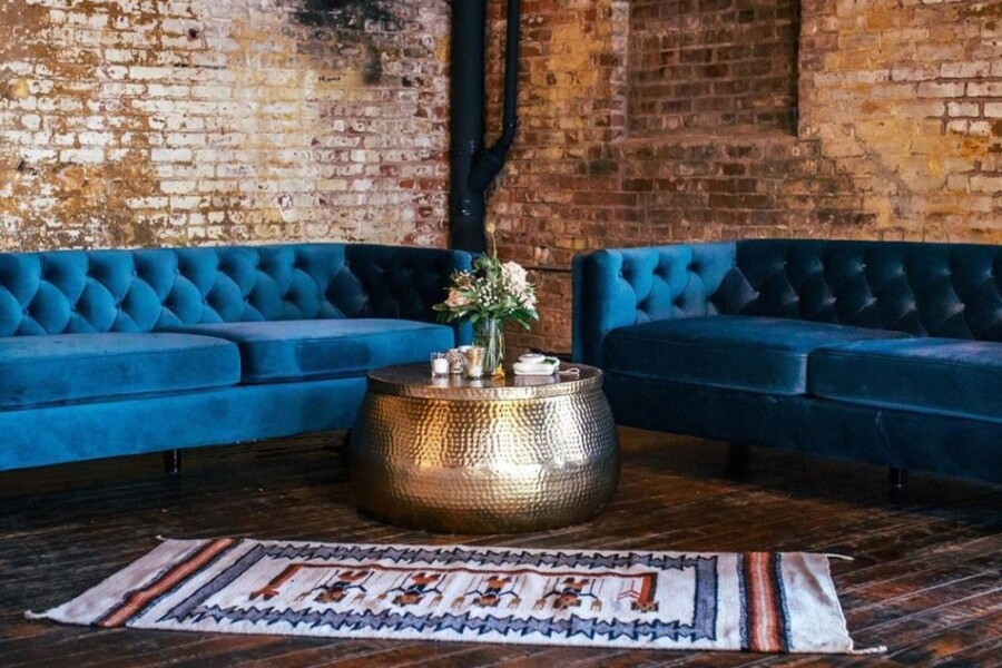 Seating area with Blue velvet couches in front of brick walls and black ductwork