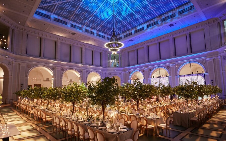 Large ornately decorated wedding reception with green trees, candles and tableware