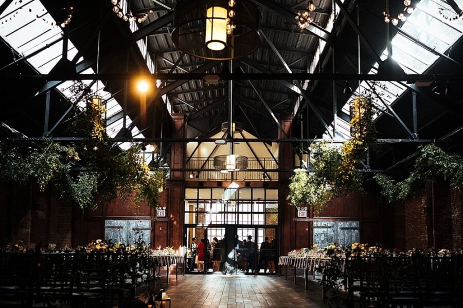 Large open industrial wedding venue decorated with flowers and plants