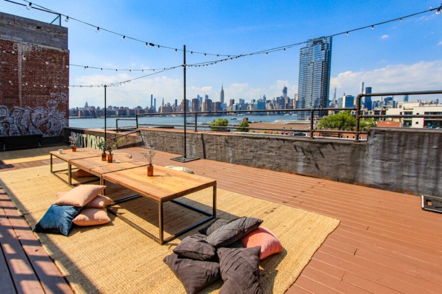 Roof seating area with pillows, tables and string lighting over looking river.