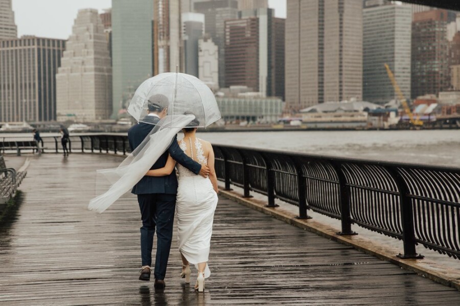 Bride and Groom walking under umbrella in rain along boardwalk by river
