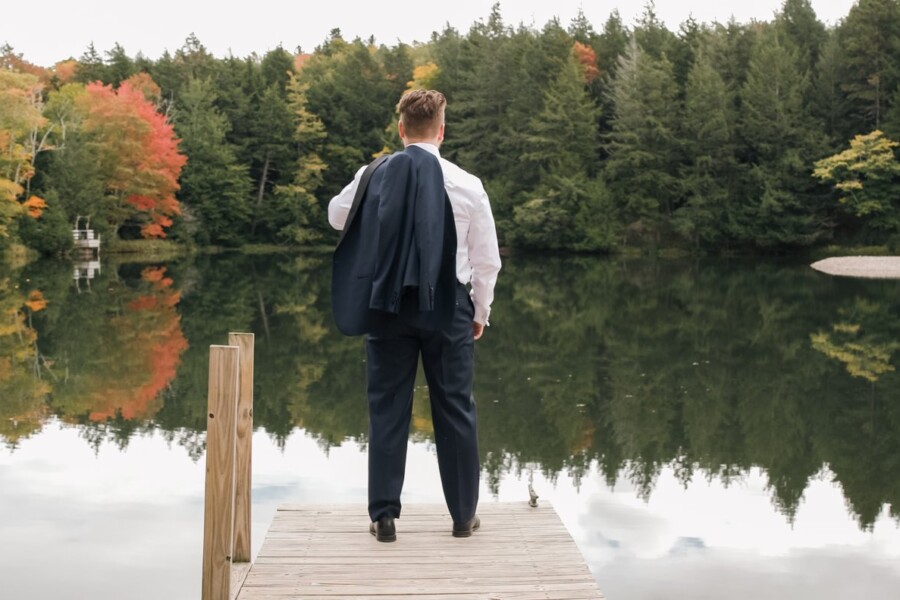 groom looking out over still lake in fall