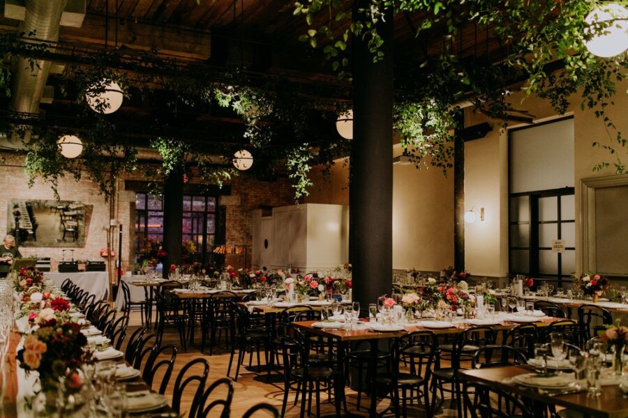 Wedding reception with plants hanging from ceiling and wooden tables decorated with flowers and tableware