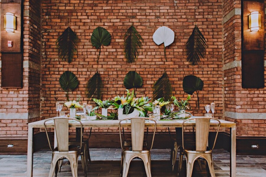 Wedding table in front of brick wall with palm branches hanging
